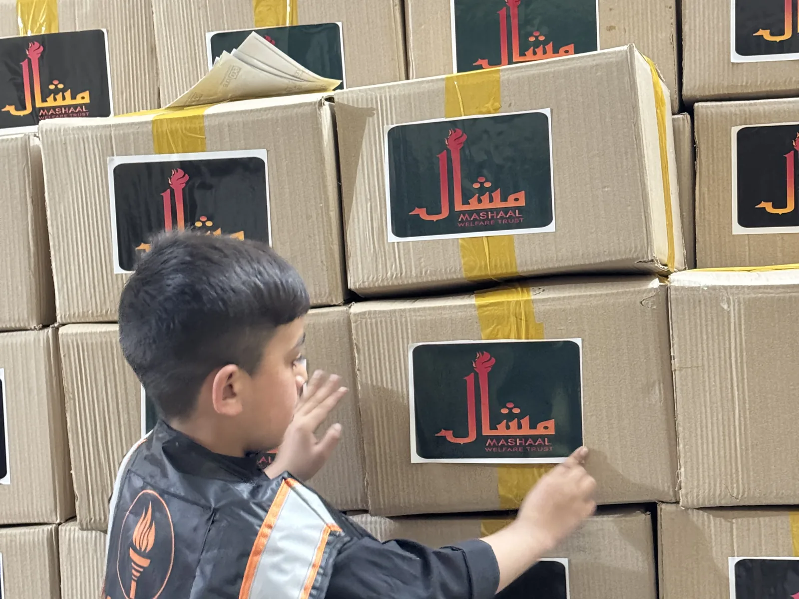 Ration packages stacked for distribution, each box marked with the Mashaal Welfare Trust logo.