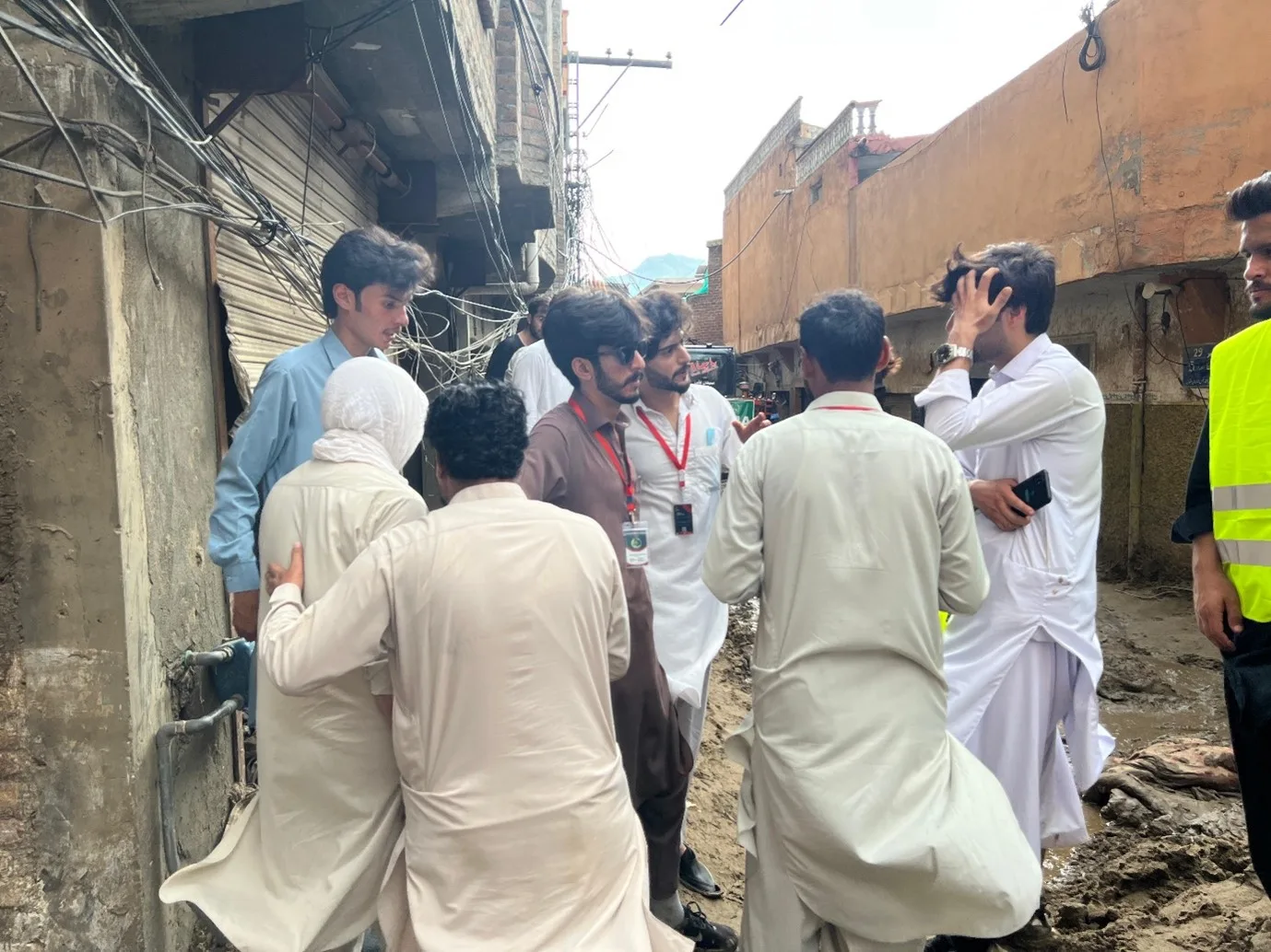 Volunteers in Mashaal lanyards helping a woman through a street left deep in flood mud.